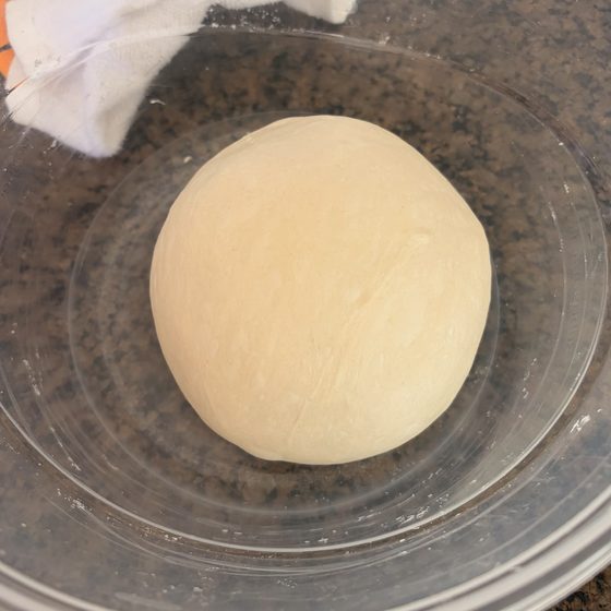 A smooth round ball of sourdough dough proofing in a covered glass bowl.