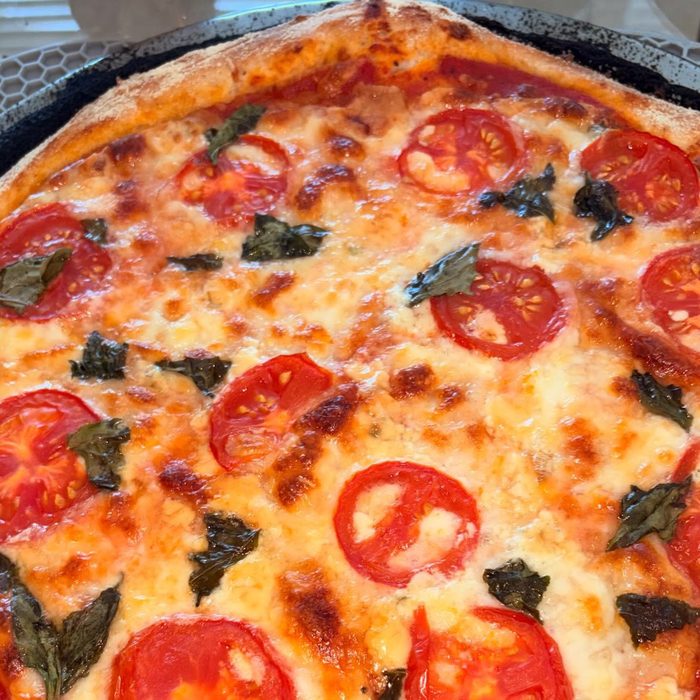 Close view of a margherita pizza with bubbling cheese, tomato slices and basil leaves.