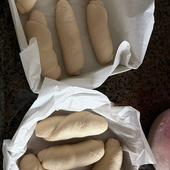 Trays of shaped pão francês dough resting on parchment before baking.